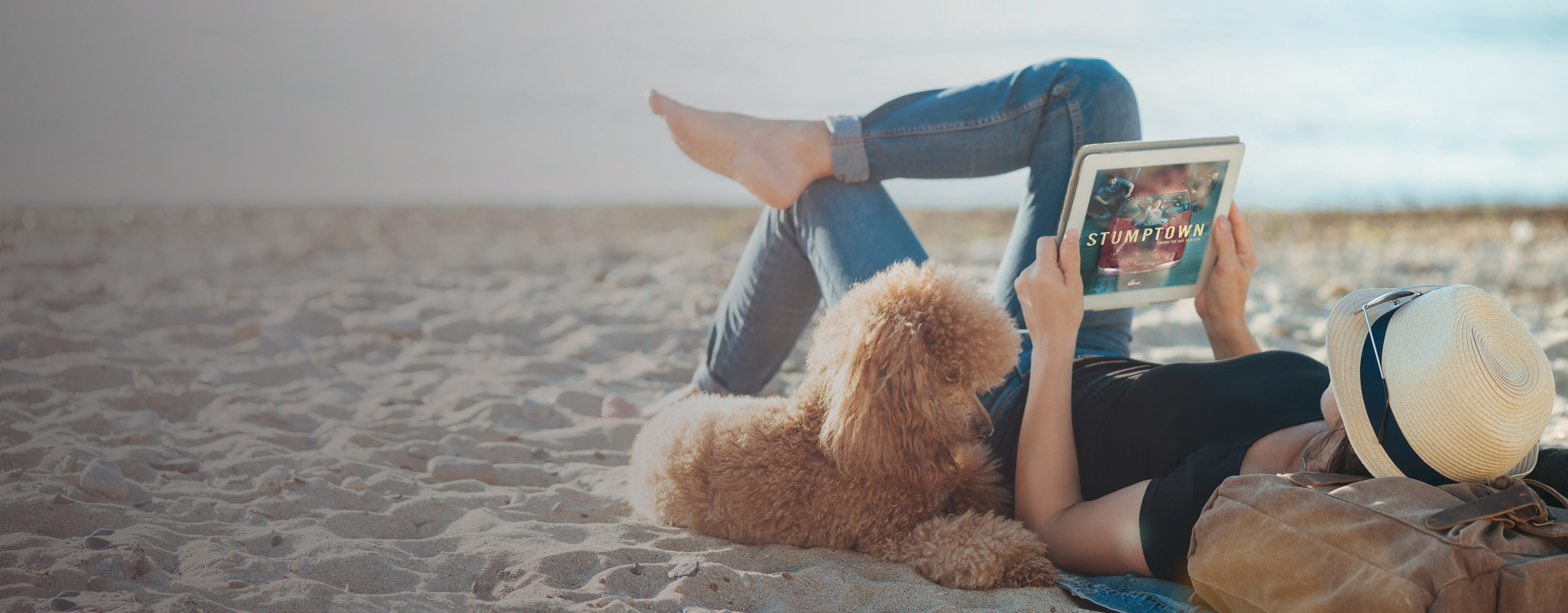 Woman lying on beach with dog and watching TV Everywhere from Northland on tablet